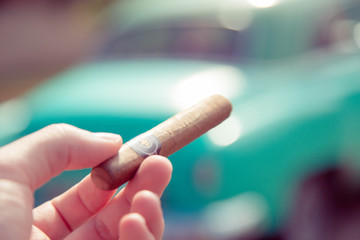 Close-up on a Hand Holding a Cuban Cigar with Vintage Car in the Background