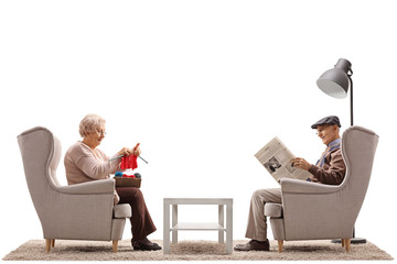 Seniors sitting in armchairs with one of them knitting and the other reading a newspaper