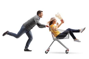 Young man pushing a shopping cart with a woman with a popcorn box riding inside