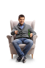 Young guy with a remote control and a beer bottle seated in an armchair