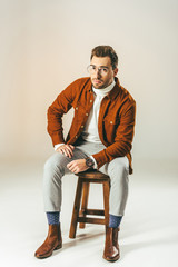 stylish man looking at camera while sitting on wooden chair, on beige