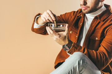 cropped shot of man putting out a cigar in ashtray isolated on beige