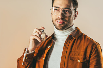 portrait of stylish young man applying perfume isolated on beige
