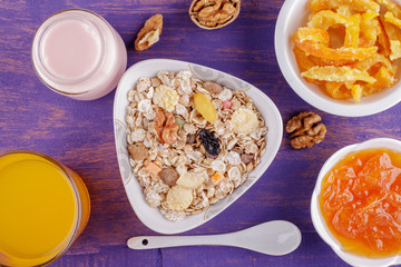 Healthy breakfast. Ceramic bowl with oat flakes, dried fruits, nuts on a violet wooden background