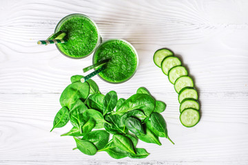 Obraz premium Green spinach and cucumber smoothie with ingredients on a white wooden background