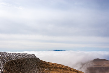 A tranquil mountain scene with clouds cover and fence on a hill. Pastel colors sky in the background