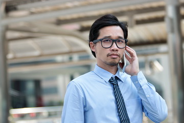 Portrait professional young Asian business man talking on phone for his job at outdoor street background.