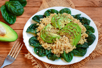 Avocado quinoa salad. Easy quinoa salad with fresh spinach leaves and avocado slices on a served plate. Brown wooden background. Rustic style. Closeup