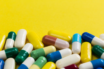 Heap of assorted colorful capsules on yellow table.