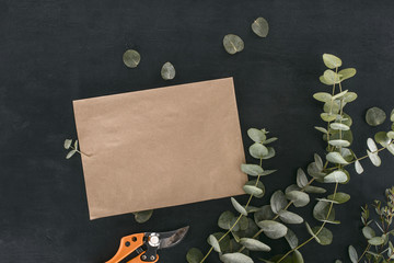 top view of blank paper envelope with garden shears and eucalyptus branches over black background