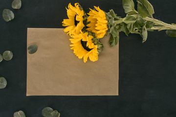 top view of blank paper envelope with sunflowers over black background