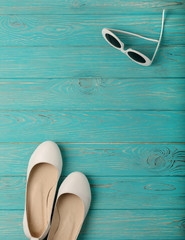 Women's shoes and white sun glasses on a blue wooden background.