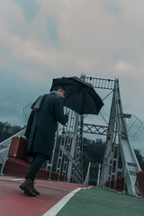 bottom view of handsome middle aged man with umbrella and luggage walking by pedestrian bridge