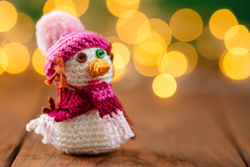 Handmade knitted snowman toy on wooden background with bokeh