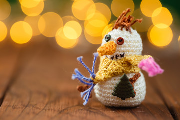 Obraz premium Handmade knitted snowman toy on wooden background with bokeh