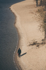 high angle view of man in coat with suitcase walking by sandy beach in autumn