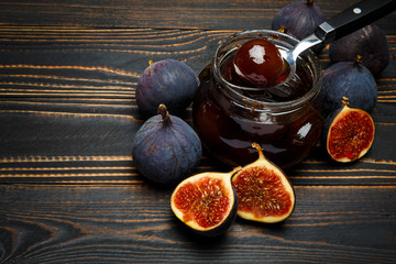 Glass jars full of fig jam and fig fruits on a dark wooden background