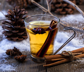 Hot winter beverage with cinnamon, anise and lemon. Winter scene with pine cones and snow.
