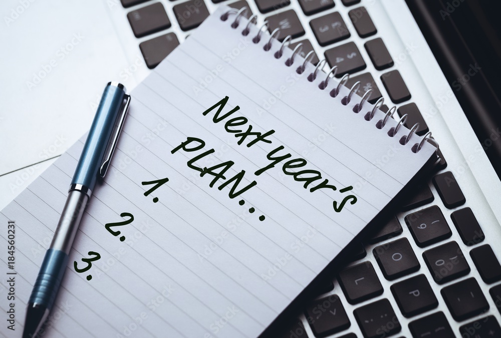 Poster top view of new years resolution written on notepad with pen on side laying on laptops keyboard
