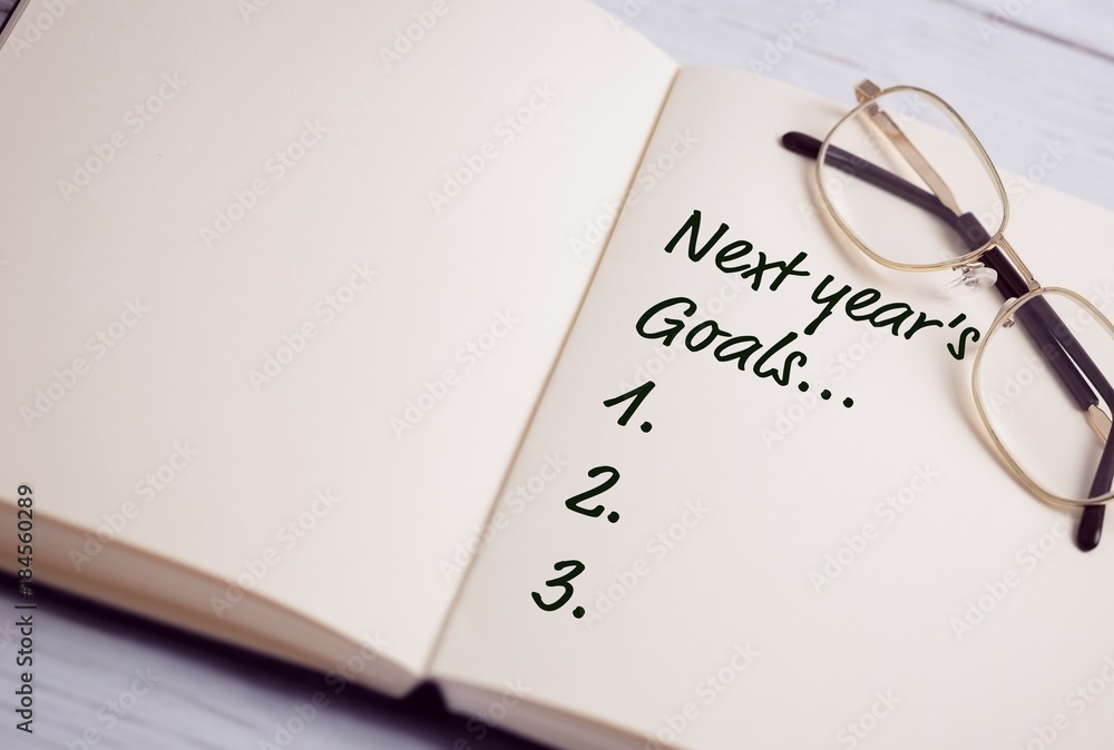 Poster top view of new years resolution written on notepad with glasses on side