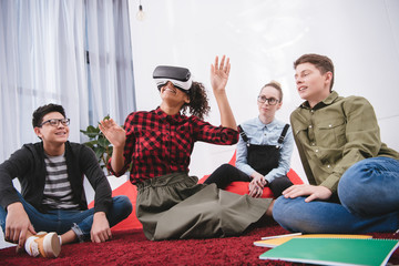 Fototapeta premium young girl in virtual reality glasses sitting on carpet with friends