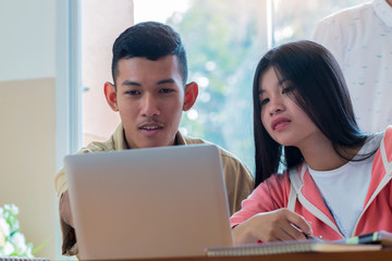 Two Asian College of students using laptop, tablet, studying together with notebooks documents paper for report near windows in classroom. Happy young study for school assignment, Education Concept