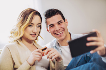 Young couple sitting on sofa and doing online shopping with tablet and credit card in room