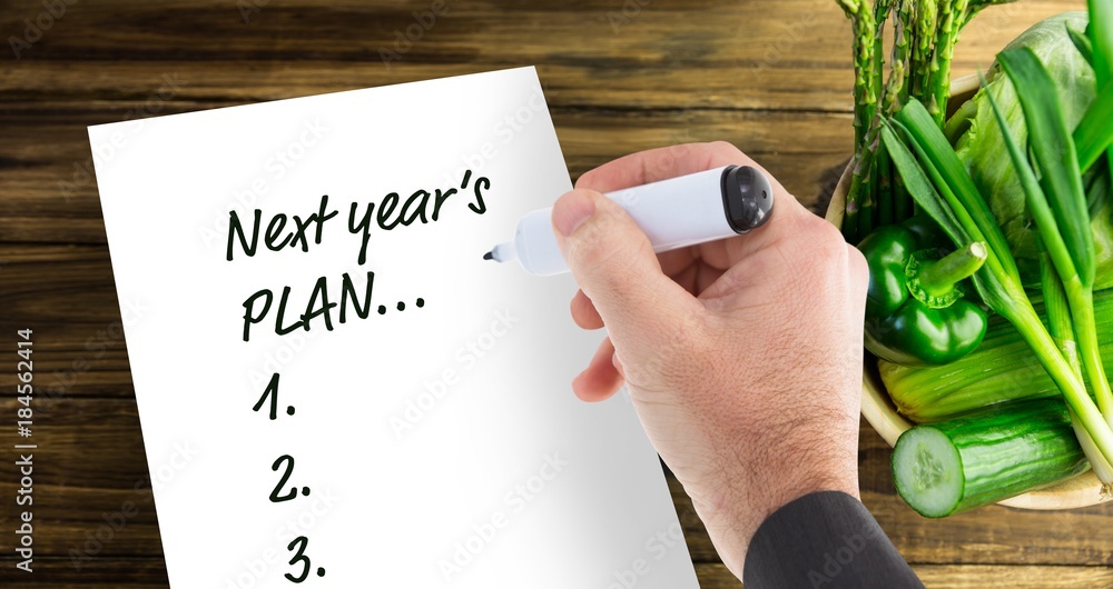 Poster top view of hand with marker writing new years resolutions on notepad and fresh vegetables next to i