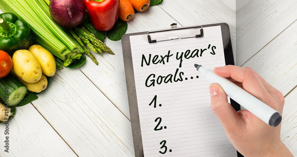 Poster top view of hand with marker writing new years resolutions on notepad and fresh vegetables next to i