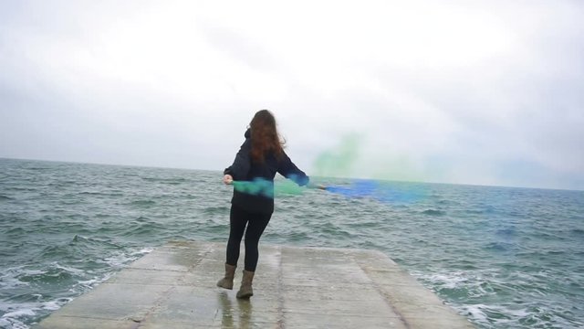 Young teenage girl playing with blue and green smoke grenades on seaside