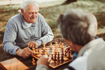 Active retired people old friends and free time two senior men having fun and playing chess at park...