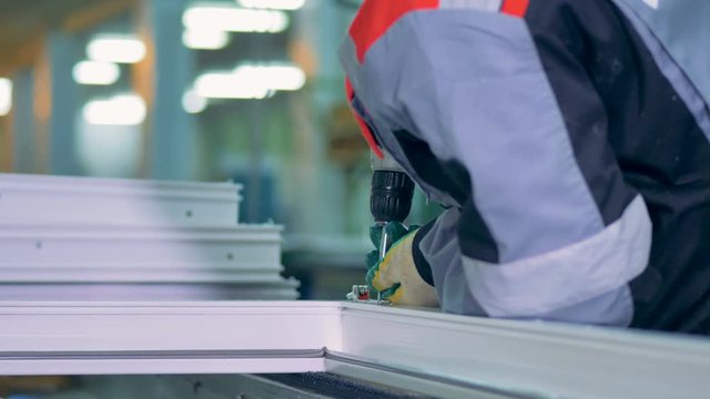 Worker assembling PVC doors and windows using industrial screwdriver.