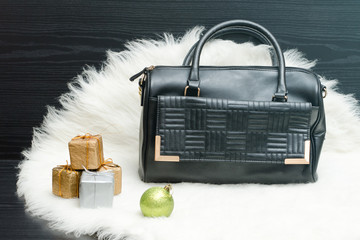 Black bag and gift box on white fur. Fashionable concept. Holiday shopping