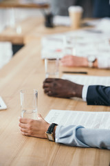 cropped shot of businesspeople sitting with glasses of water in conference hall