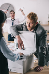 businessman helping colleague with copier at office