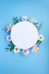 Frame of chamomiles, branches, leaves and lilac petals on blue background. Flat lay, top view