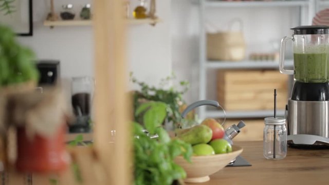 Close-up video of vege woman pouring water into blender with green smoothie with kale and avocado on wooden countertop