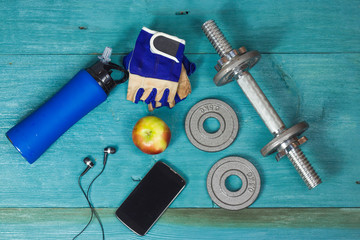 Weight plates, gloves and smartphone on wooden background