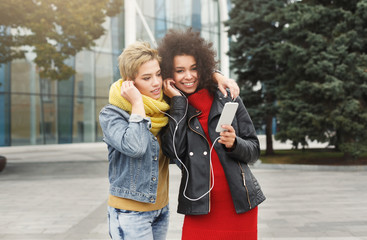 Happy female friends listen to music outdoors