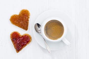 toasts in heart shape with fruit jam and cup of coffee on white wooden background