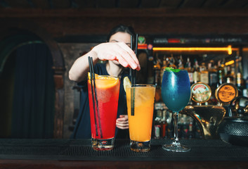 The barman decorates alcoholic cocktails. Beautiful alcoholic cocktails at the bar stand. Cocktails on the background of a bartender.
