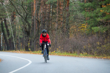 Obraz premium Young Woman in Orange Jacket Riding Road Bicycle in the Park in the Cold Autumn Day. Healthy Lifestyle.