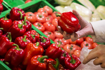 the girl is shopping at the grocery store and takes a red sweet bell pepper in her hand