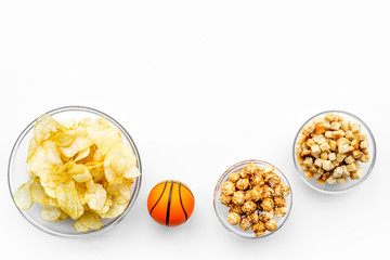 Snacks for watching sport matches and games on TV. Crisps, popcorn, rusks near ball on white background top view copyspace
