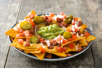 Mexican nachos with beef, guacamole, cheese sauce, peppers, tomato and onion in plate on wooden table


