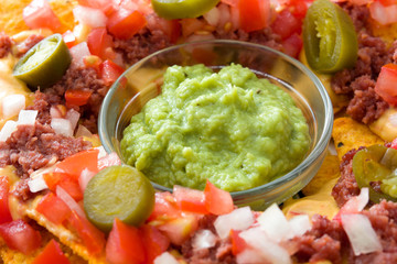 Mexican nachos with beef, guacamole, cheese sauce, peppers, tomato and onion background

