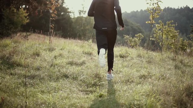 Slow motion. Man running on autumn grass hill. Camera follows cross country runner enjoying atmospheric fall nature.