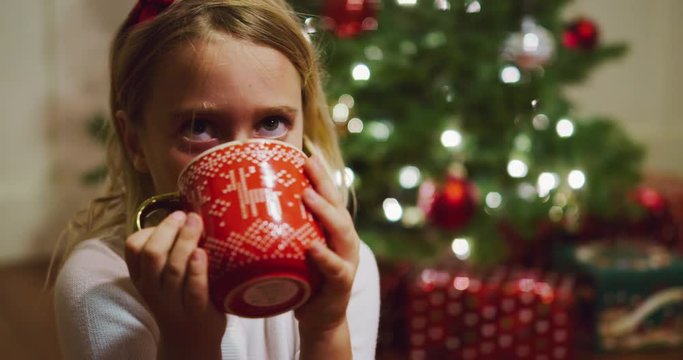Cute young girl eating Christmas cookies and drinking hot chocolate