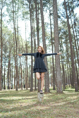 Beautiful asia woman with brown hair standing on one leg on stump in pine park