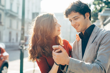 Young beautiful couple in love using smart phone together outdoor in the city - interaction, love, technology concept